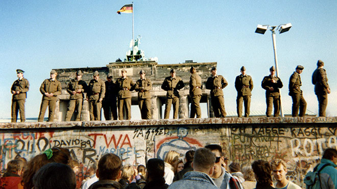 11 نوفمبر 1989 ، يقف حرس الحدود من ألمانيا الشرقية على جزء من جدار برلين مع بوابة براندنبورغ في الخلفية في برلين
